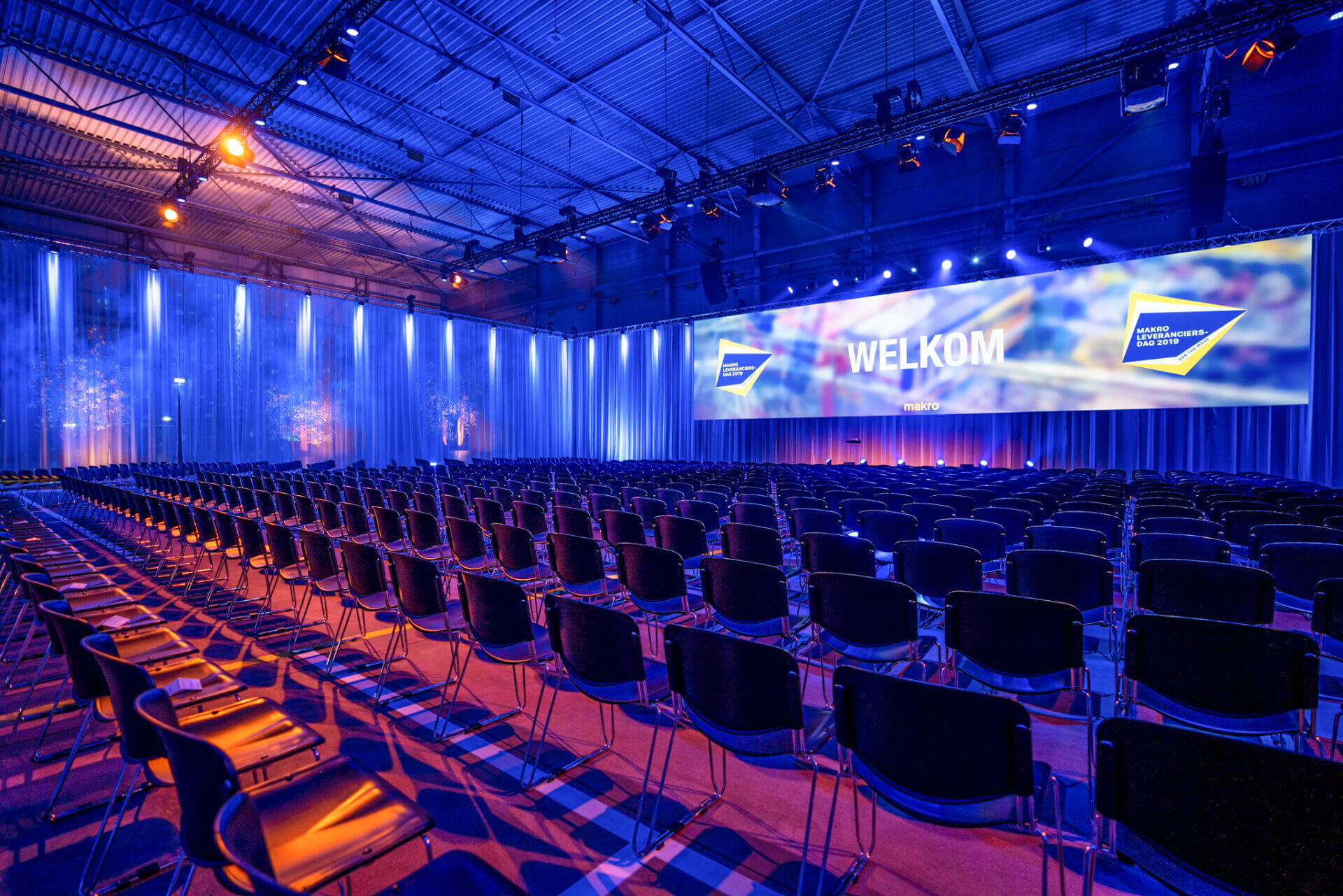 loods omgetoverd tot congreszaal met groot scherm en veel stoelen